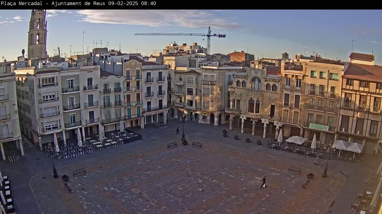 A mostly empty town square with several multi-story buildings surrounding it, under a clear, sunrise sky.