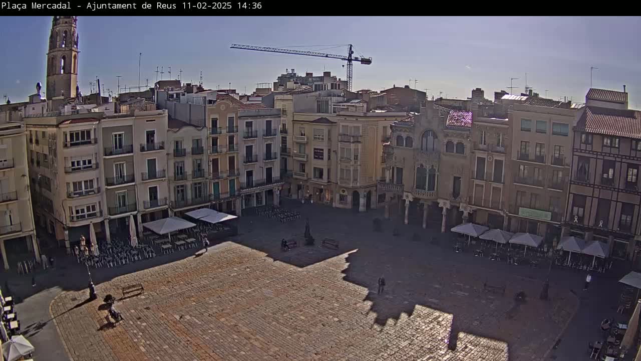 A mostly empty cobblestone town square is surrounded by multi-story buildings under a clear, sunny sky.