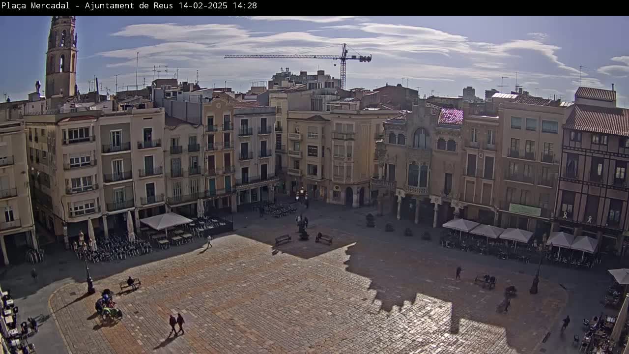 A large, paved town square is surrounded by multi-story buildings under a partly cloudy sky.