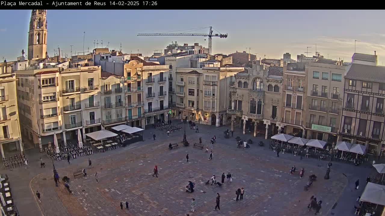 A large town square, populated with a few people, is surrounded by multi-story buildings under a clear, twilight sky.
