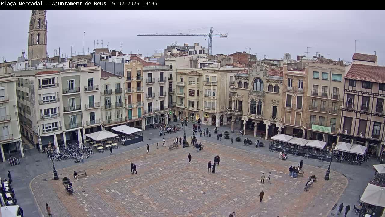 A large, paved town square is surrounded by multi-story buildings under an overcast sky.