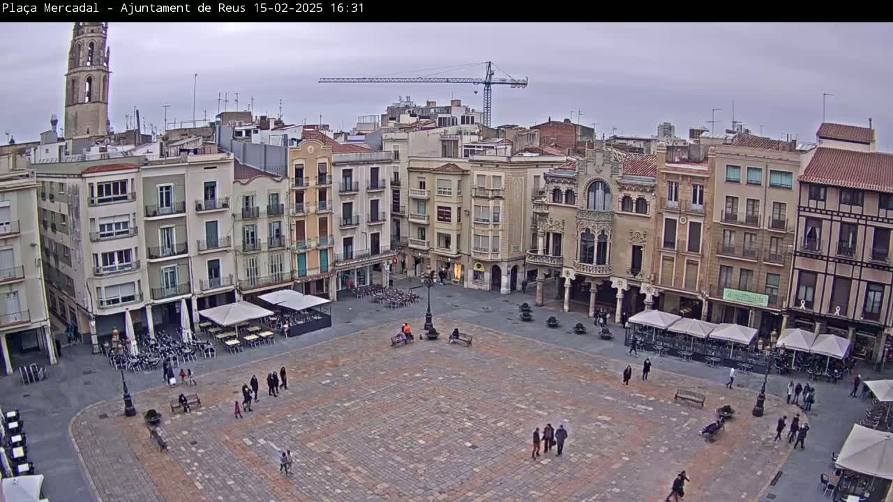 A large, mostly empty town square with several multi-story buildings surrounding it under an overcast sky.