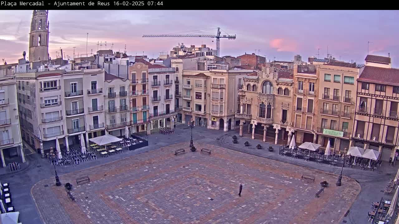 A large, paved town square, surrounded by multi-story buildings, is mostly empty under a pale pink and purple sunrise sky.