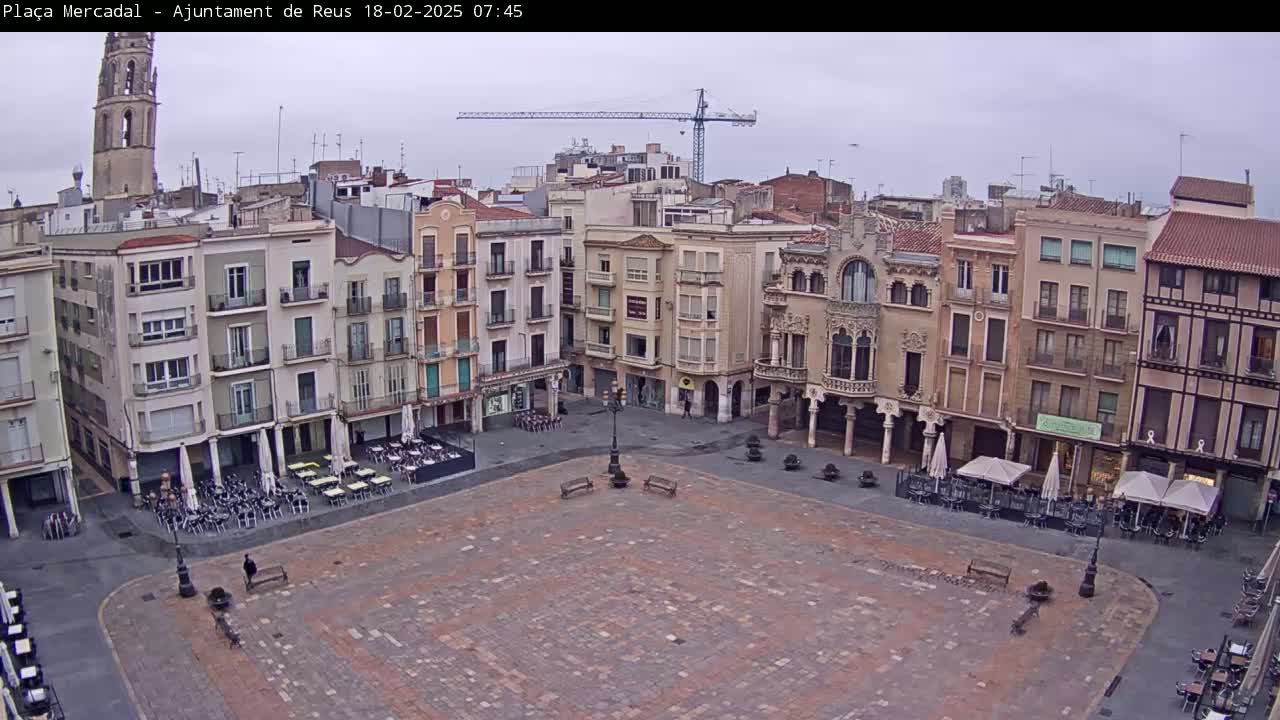 A large, mostly empty town square with multiple-story buildings surrounding it under an overcast sky.