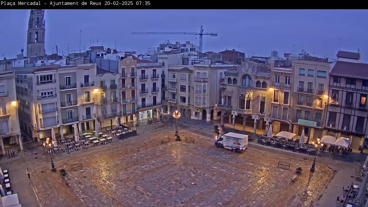 A large, mostly empty cobblestone town square is surrounded by multi-story buildings at twilight under a clear, dark blue sky.