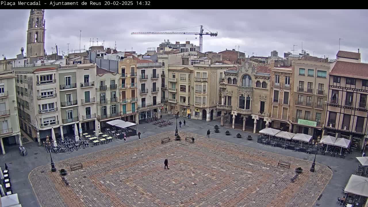 A large, cobblestone town square is surrounded by multi-story buildings under an overcast sky.