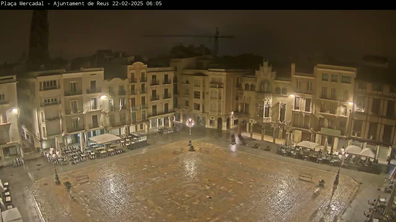 A rain-slicked, cobblestone town square at night, surrounded by multi-story buildings with illuminated outdoor seating areas.