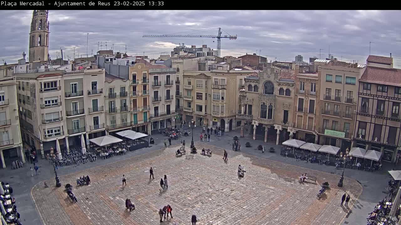 A large, cobblestone town square is surrounded by multi-story buildings under an overcast sky.