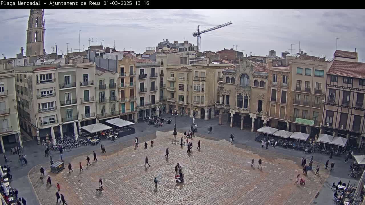 A large, paved town square with several buildings surrounding it, some with outdoor seating, under an overcast sky.