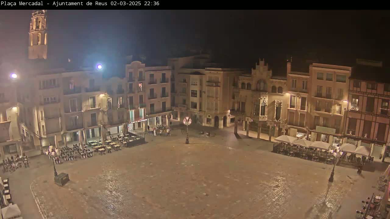 A nighttime, high-angle view of a town square with several buildings surrounding it, some with outdoor seating areas.