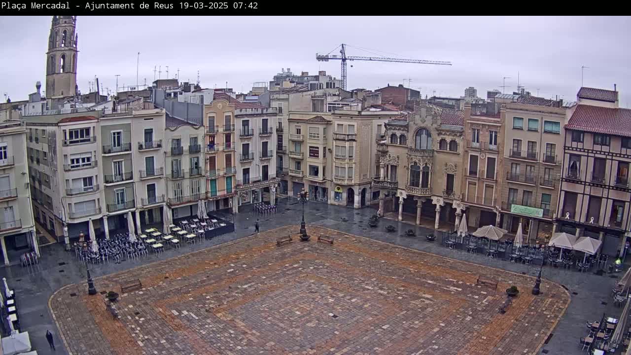 A mostly empty town square with several multi-story buildings surrounding it is shown on a cloudy day.