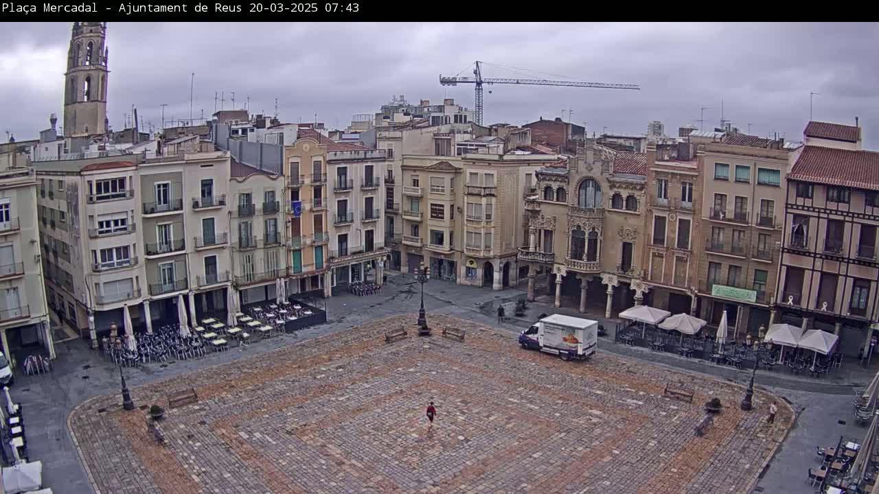 A large, paved town square, surrounded by multi-story buildings, under an overcast sky.