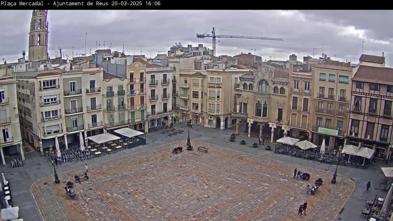 A large, paved town square is surrounded by multi-story buildings under an overcast sky.