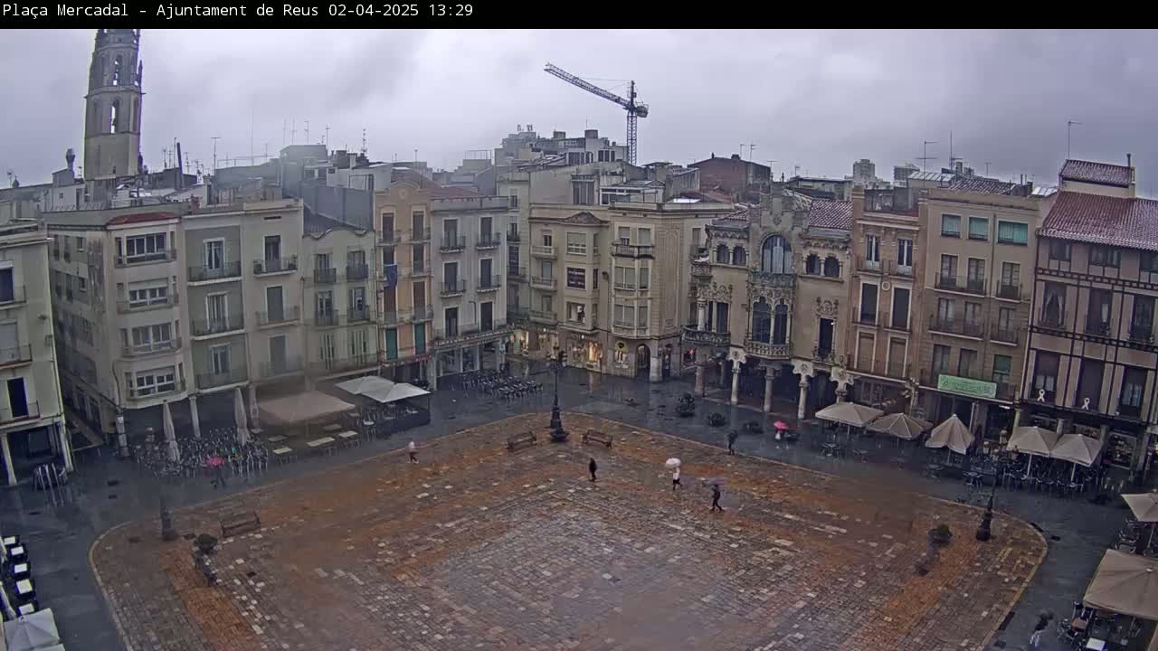 A town square, surrounded by multi-story buildings, is shown on an overcast day with light rain.