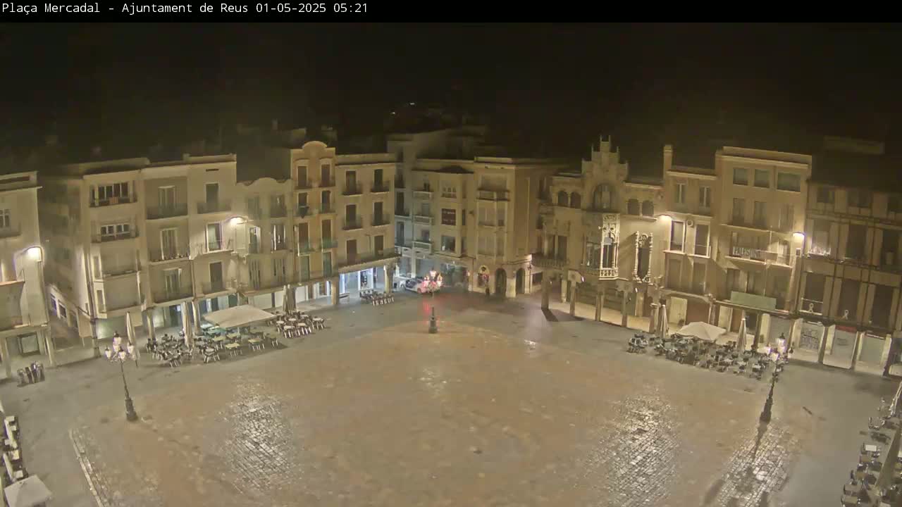 A wet, empty town square at night, surrounded by multi-story buildings with lights on.