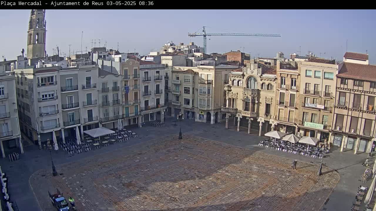 A large, mostly empty town square with several buildings surrounding it, under a clear, sunny sky.