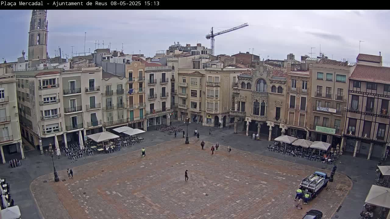 A large, mostly empty town square with surrounding buildings under an overcast sky, and a construction crane visible in the distance.
