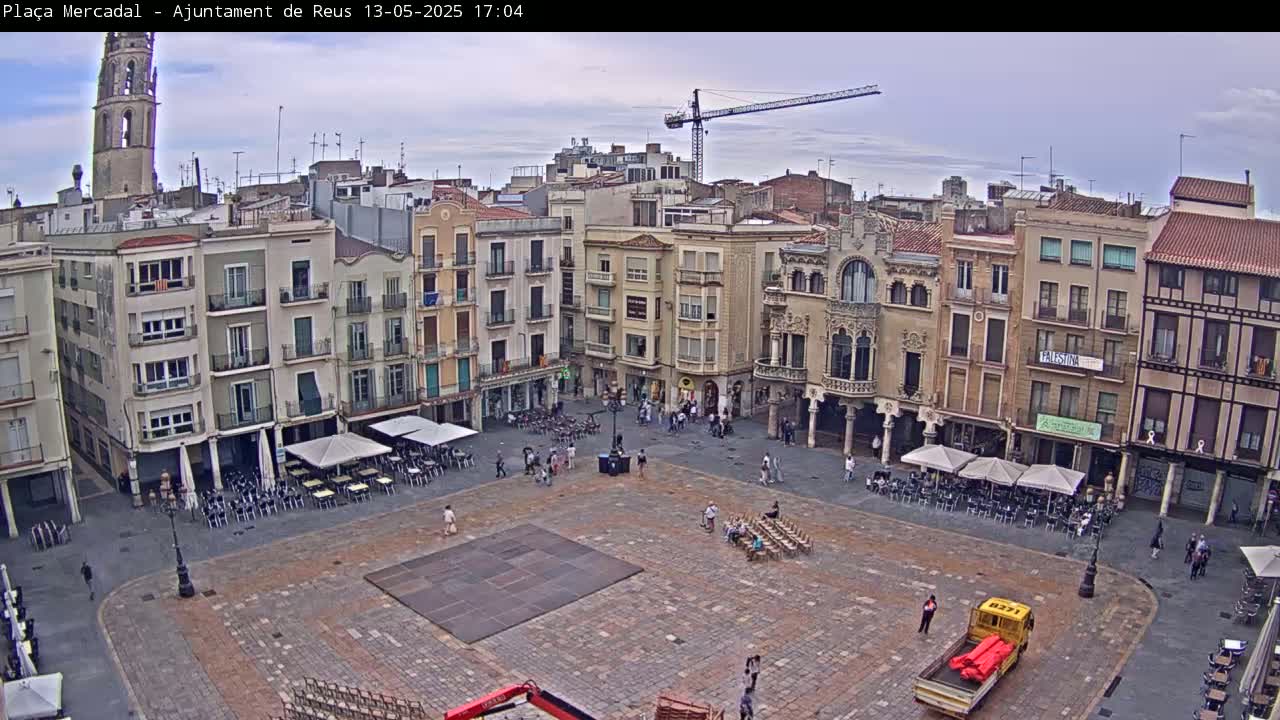 An overcast day reveals a large, mostly empty town square surrounded by multi-story buildings, with a few people scattered about and some outdoor seating areas.