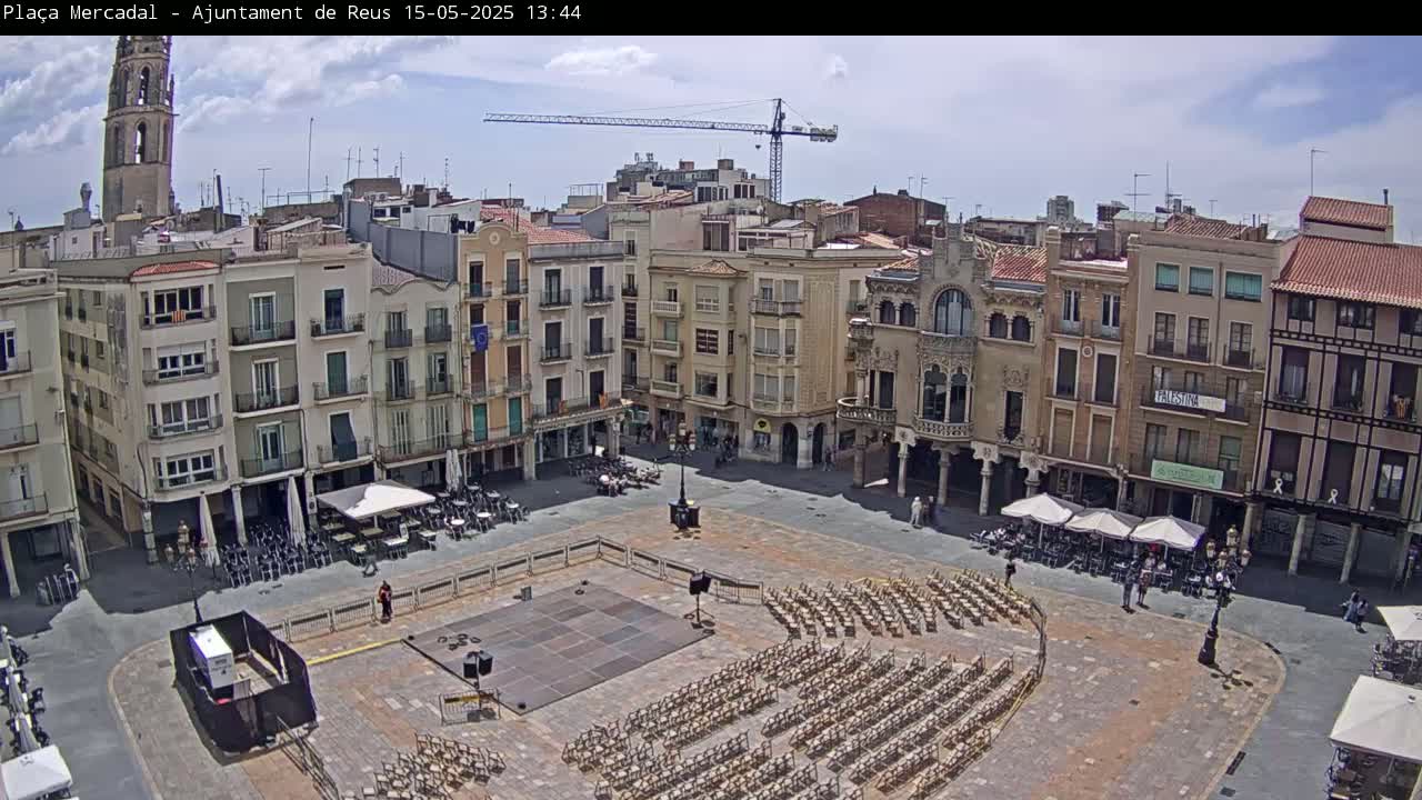 A town square with numerous buildings surrounding it, under a partly cloudy sky, is set up with rows of chairs for an outdoor event.