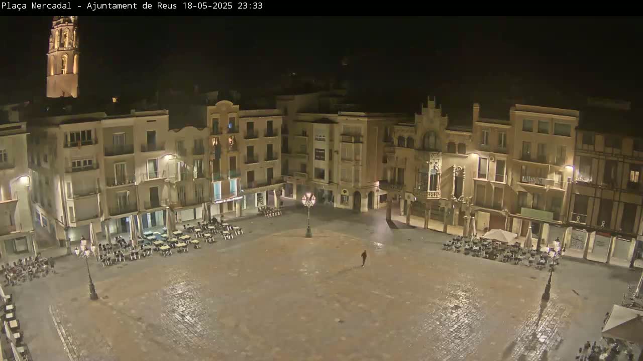 A mostly empty town square at night, surrounded by buildings with illuminated windows, under a clear, dark sky.