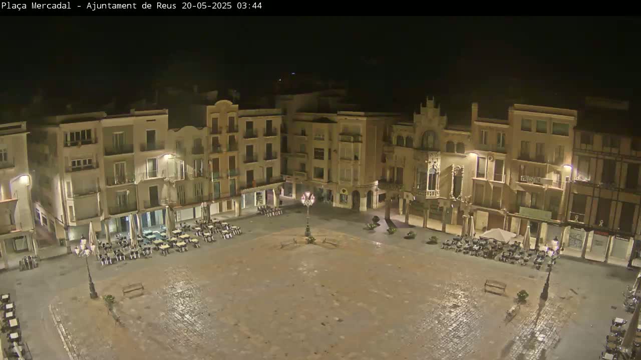 A nighttime, possibly wet, view of a town square surrounded by buildings with outdoor seating areas.
