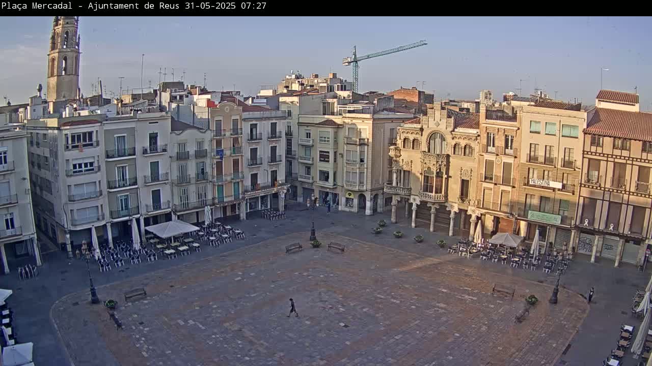 A mostly empty town square with several outdoor cafes, surrounded by multi-story buildings under a clear, light blue sky.
