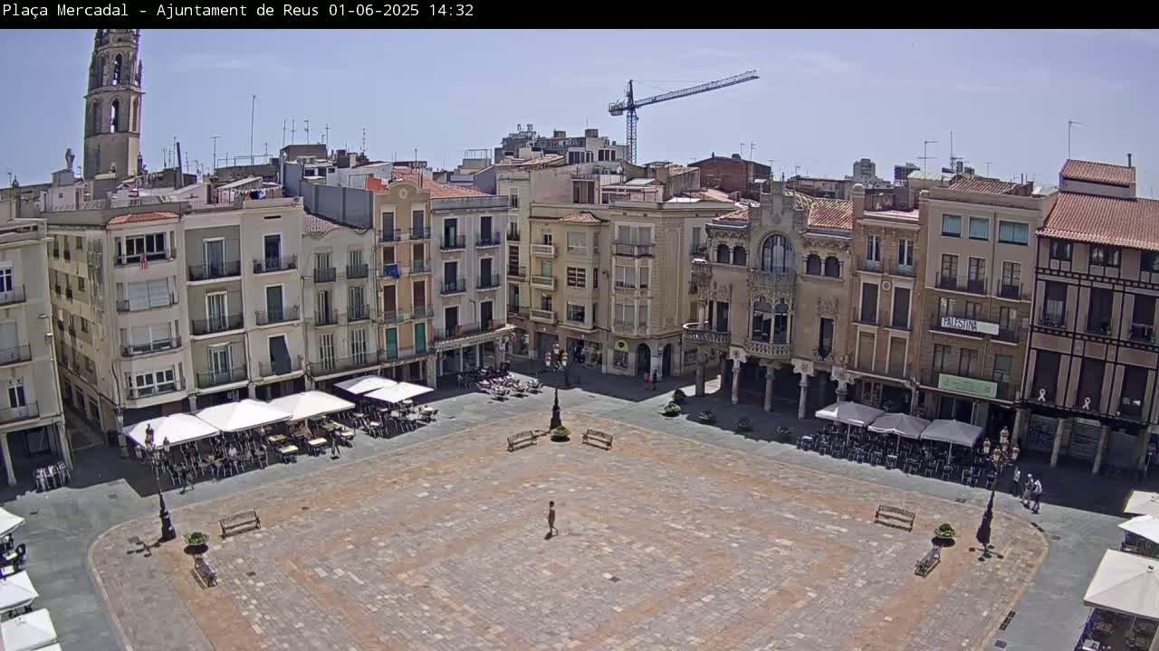 A large, paved town square with several outdoor cafes and buildings surrounding it under a clear, sunny sky.
