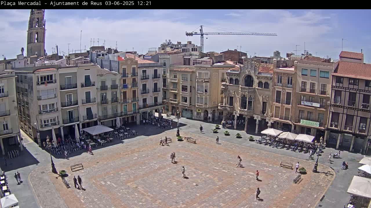 A large, mostly empty town square is surrounded by multi-story buildings under a sunny sky, with a construction crane visible in the background.