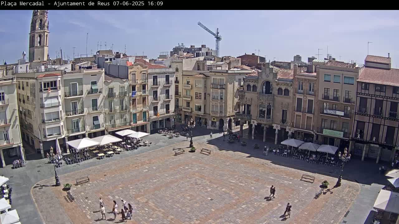 A large, mostly empty town square with several outdoor cafes, surrounded by multi-story buildings under a clear, sunny sky.
