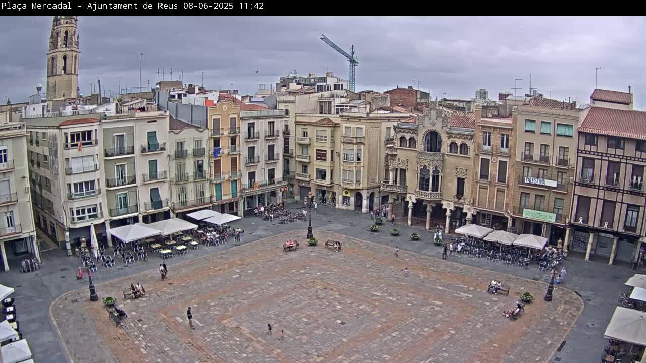 A large, paved town square with several outdoor cafes is surrounded by multi-story buildings under an overcast sky.