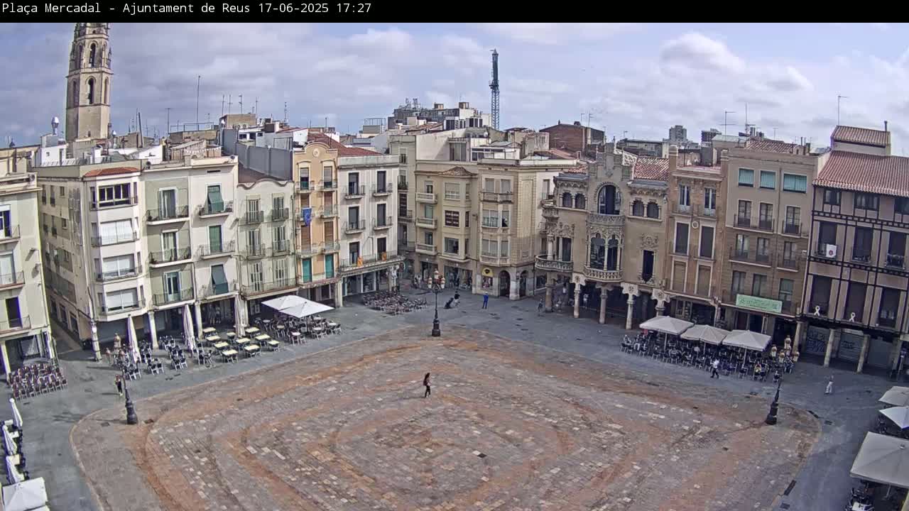 A mostly empty town square with several buildings surrounding it under a partly cloudy sky.