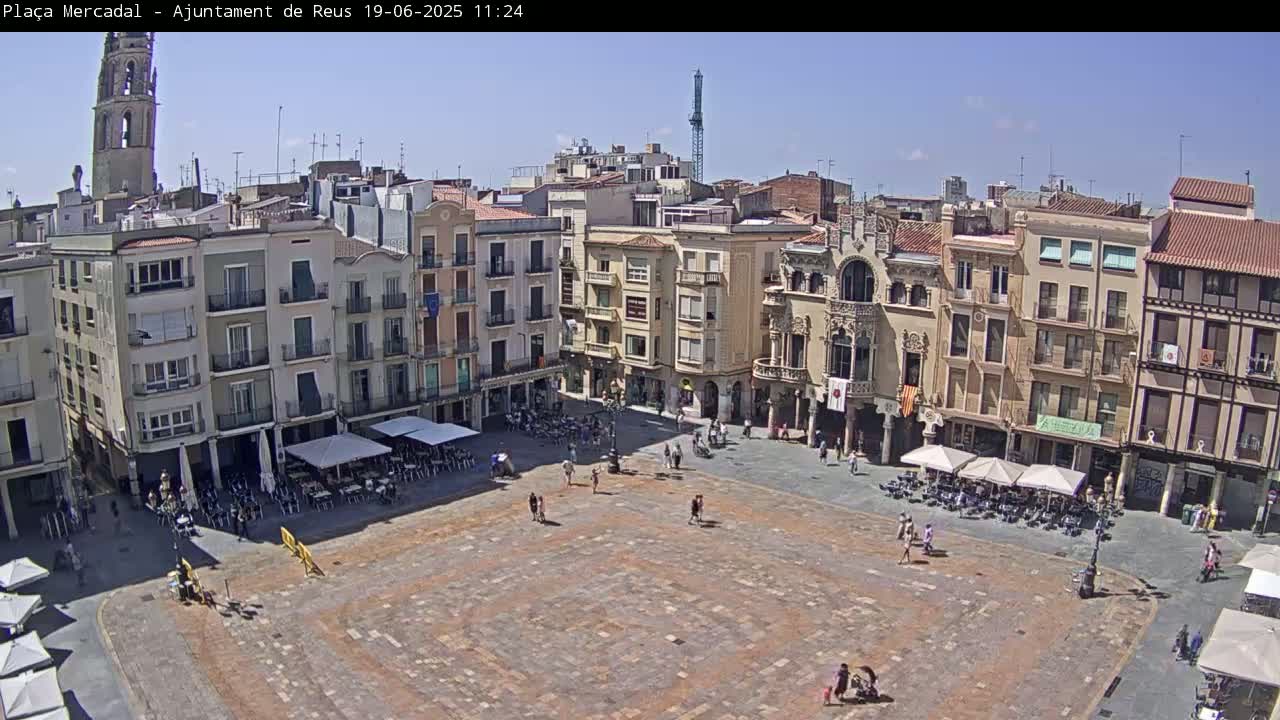 A large, mostly empty town square paved with brick is surrounded by multi-story buildings under a clear, sunny sky.