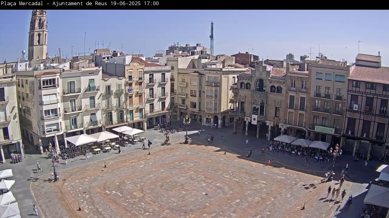 A large, mostly empty town square is surrounded by multi-story buildings under a clear, sunny sky.
