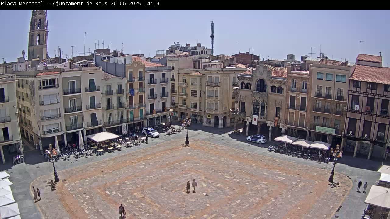 A large, paved town square is surrounded by multi-story buildings under a clear, sunny sky.