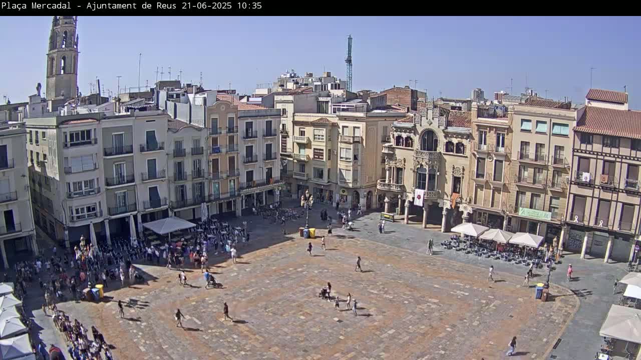 A large town square filled with people and outdoor cafes under a clear, sunny sky.