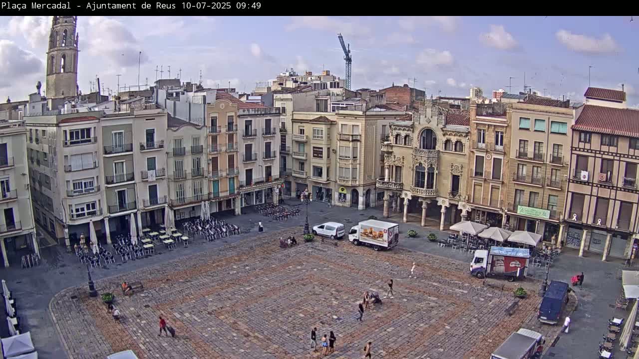 A large, cobblestone town square is surrounded by multi-story buildings under a partly cloudy sky.