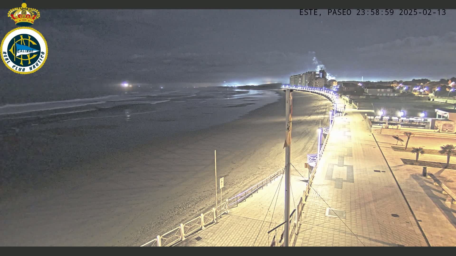 A nighttime view of a mostly empty beach and boardwalk, under a dark, cloudy sky.