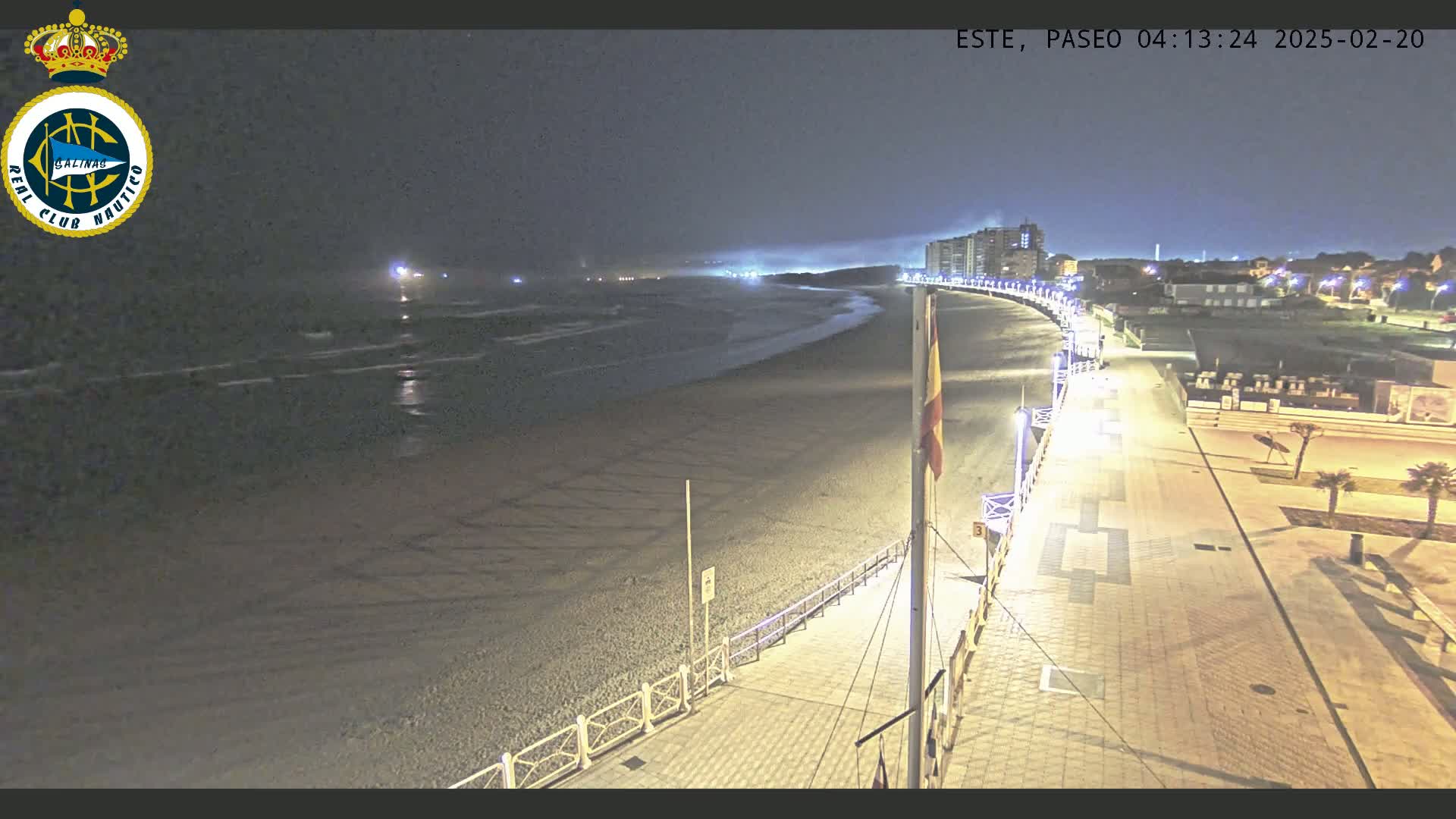A nighttime view of a dark, sandy beach and a paved boardwalk lined with lights, under a mostly clear sky.