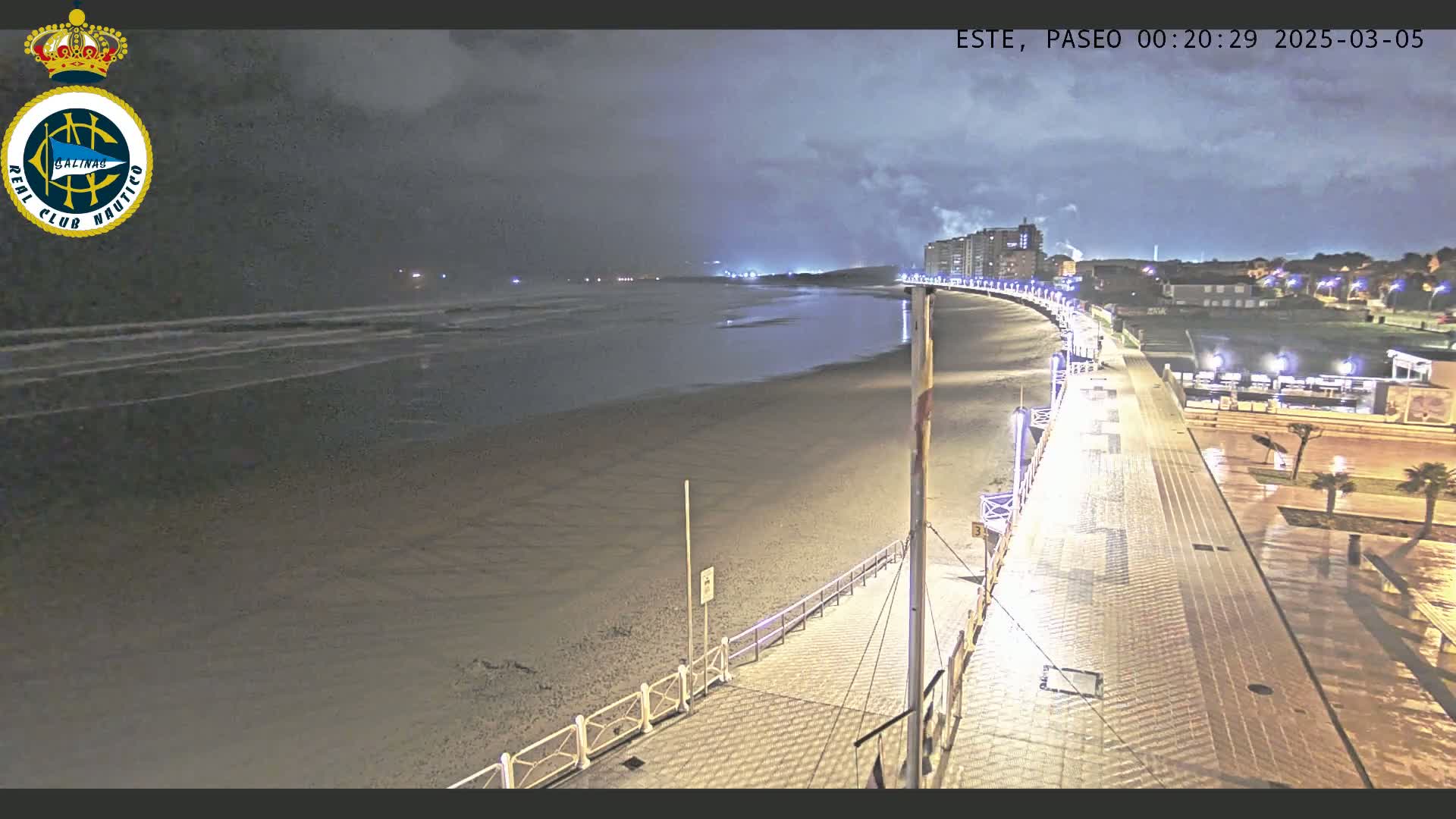 A nighttime view of a beach with a paved walkway curving alongside it, under a cloudy sky.