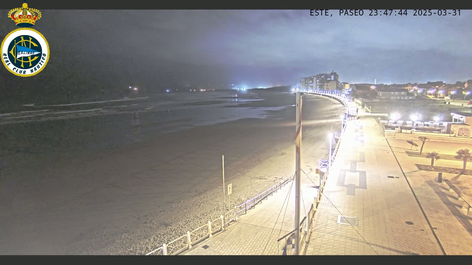 A nighttime view of a mostly empty beach and boardwalk, under a cloudy sky.