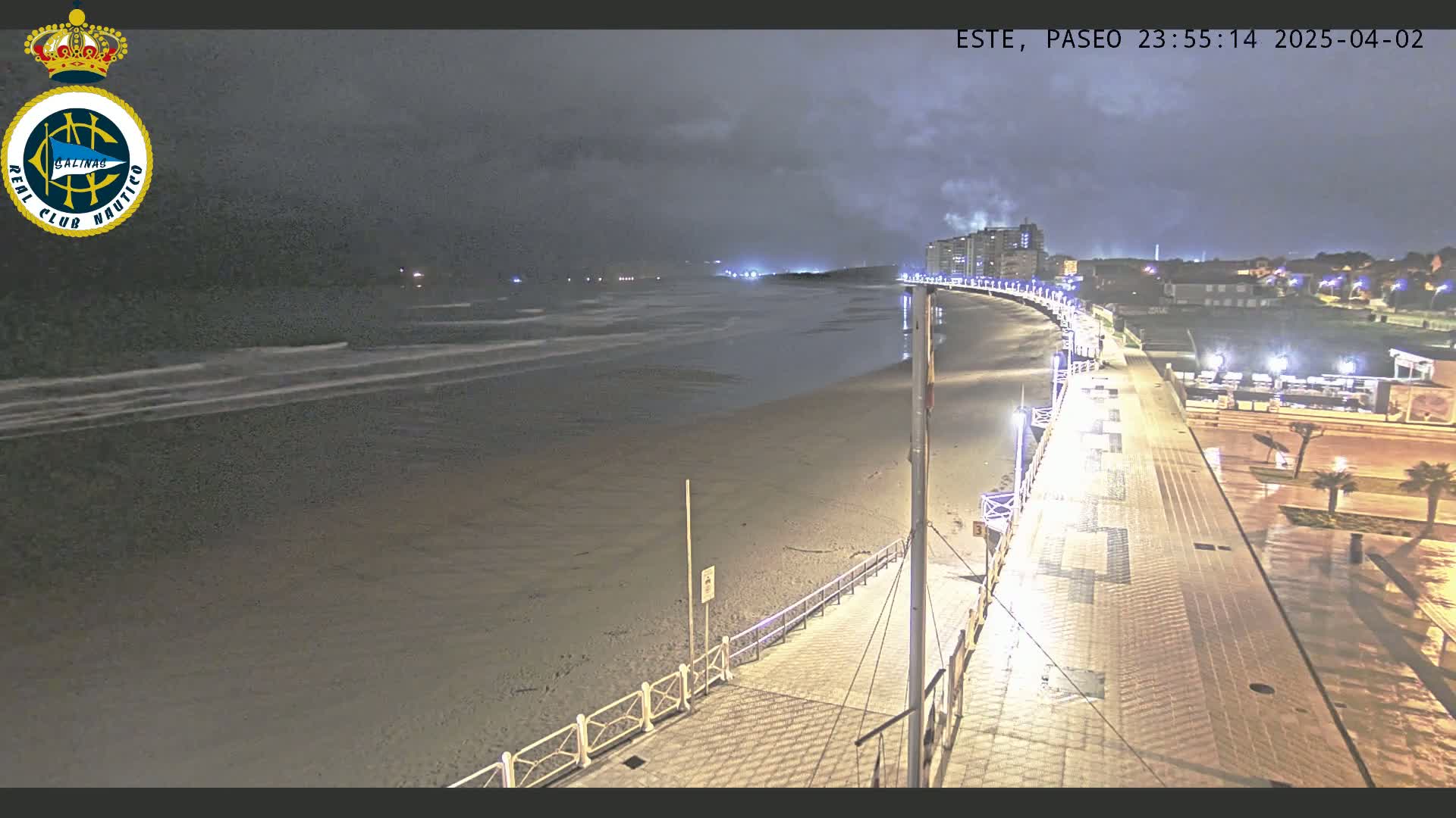 A nighttime view of a beach promenade with gentle waves under a cloudy sky.