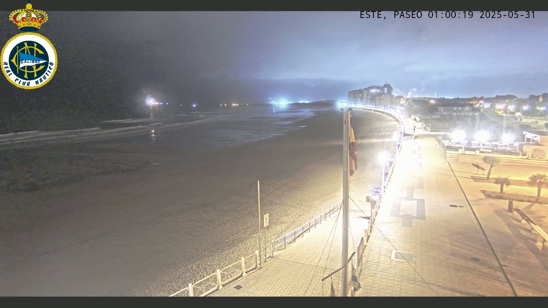 A nighttime view of a mostly empty beach and boardwalk, under an overcast sky.