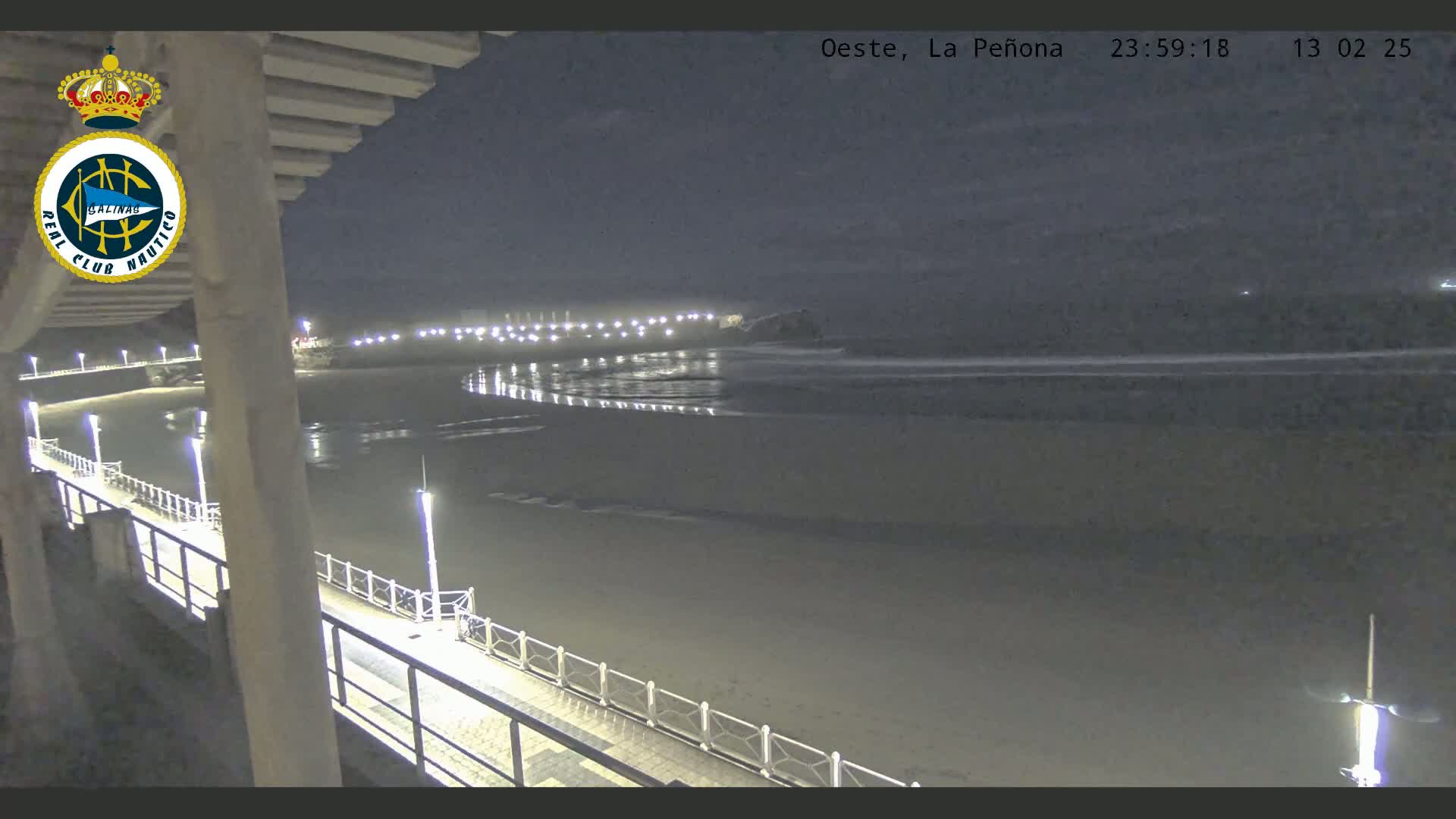A nighttime view from a pier shows a dark sandy beach and calm ocean under a clear sky.