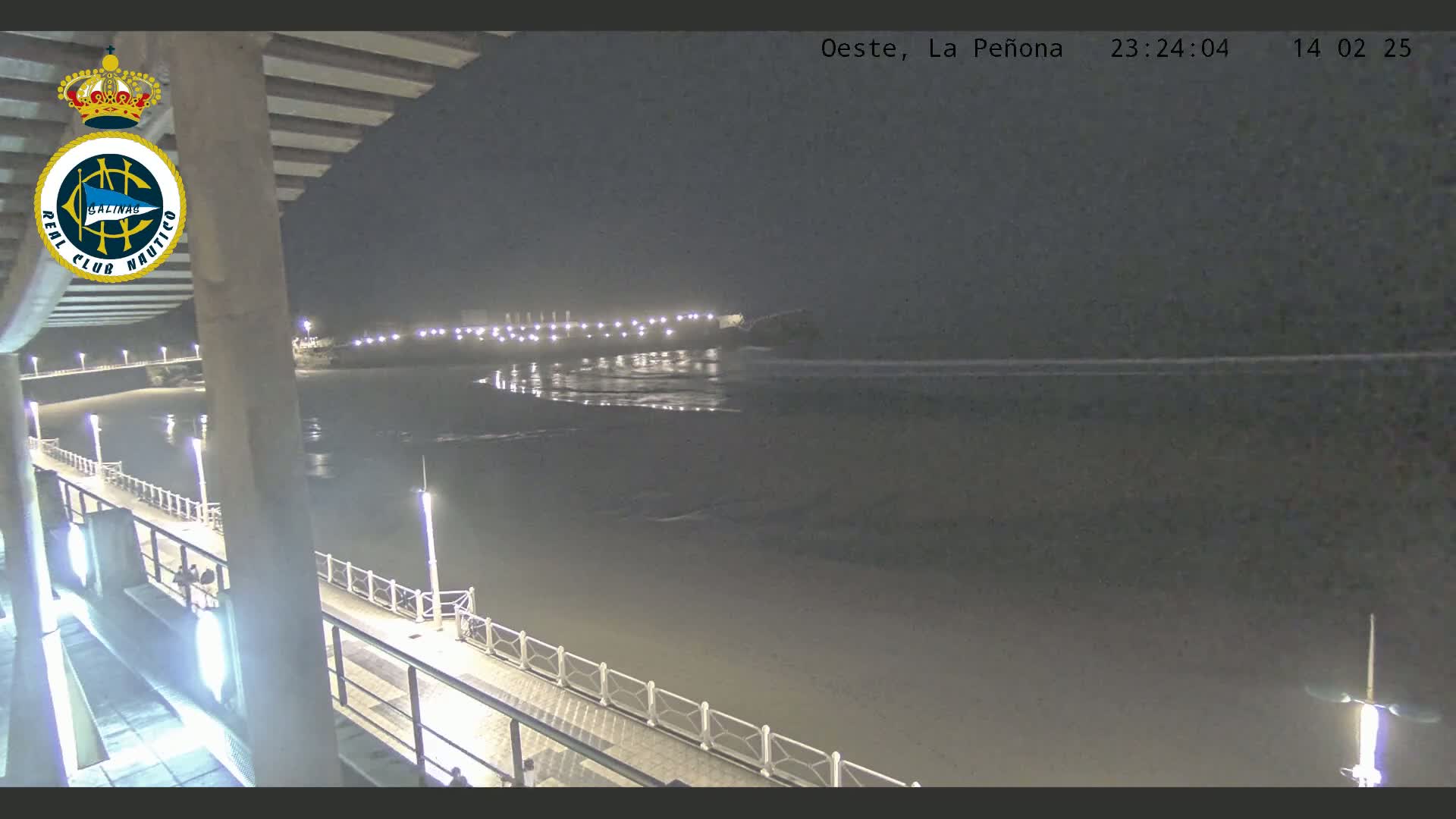 A nighttime view from a pier shows a calm, dark beach and ocean under a clear sky.