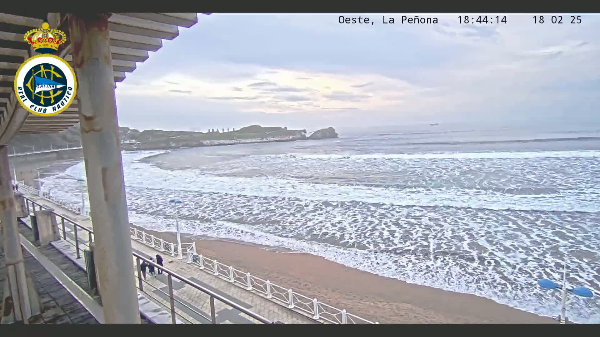 A sandy beach with moderate waves under an overcast sky is viewed from a seaside structure.