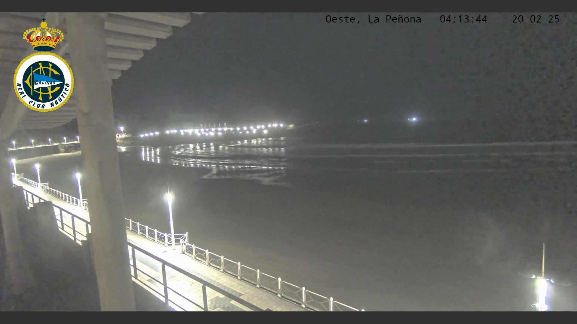 A nighttime view from a pier shows calm ocean waves lapping at a dimly lit shoreline.
