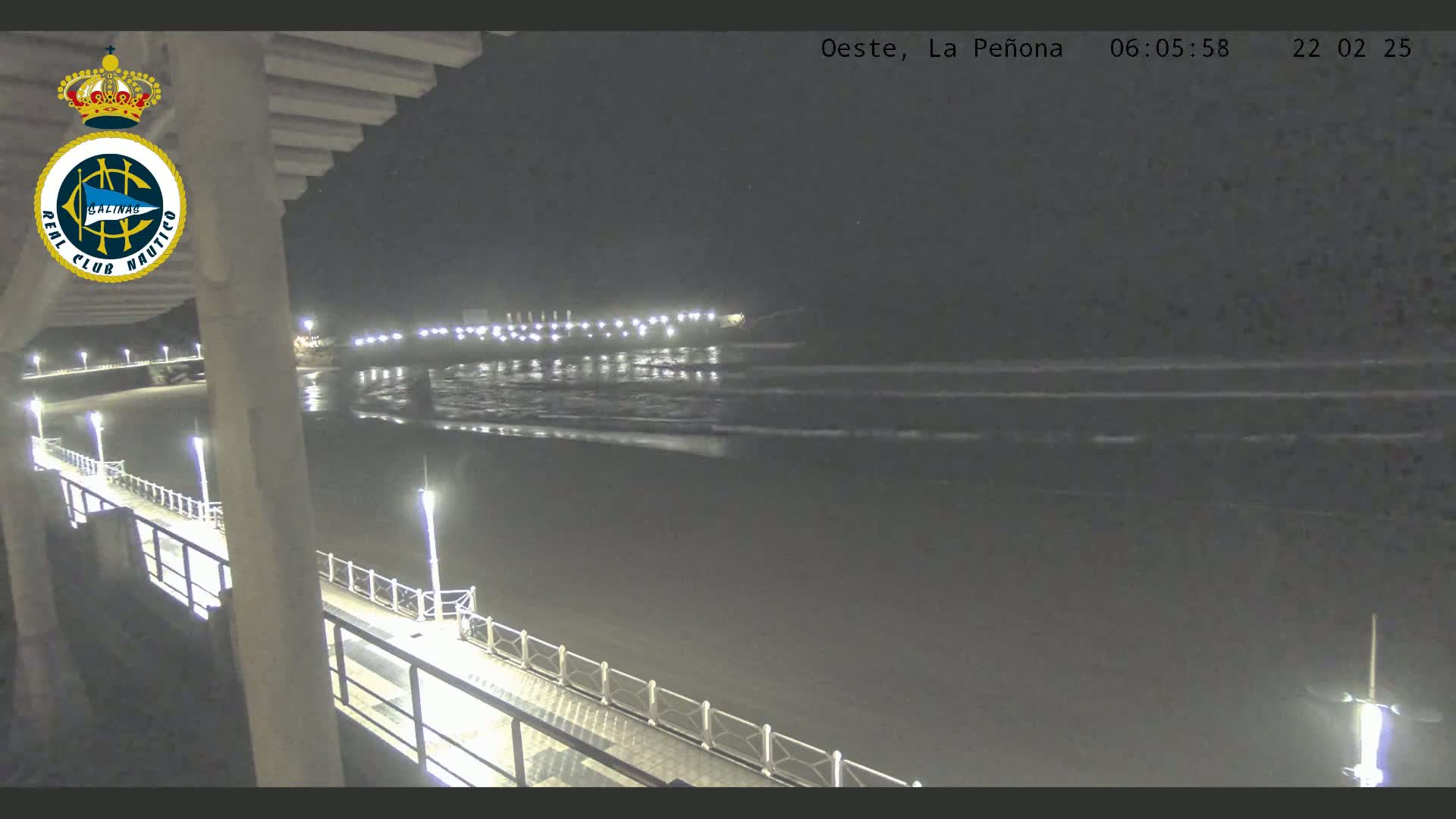 A nighttime view from a pier shows a dark beach and calm ocean waves under a clear sky.