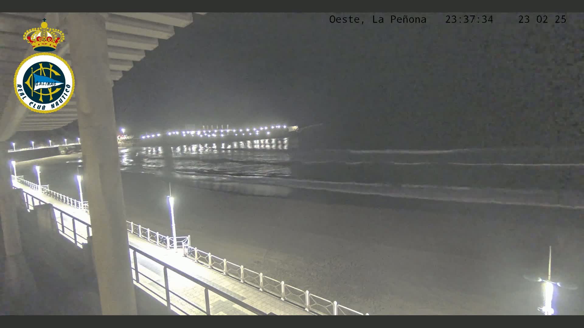 A nighttime view from a pier shows a dark sandy beach and gently rolling waves under a clear, dark sky.