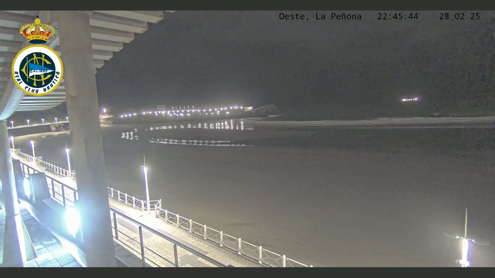 A nighttime view of a beach at low tide, with a boardwalk and lights visible, under a dark sky.