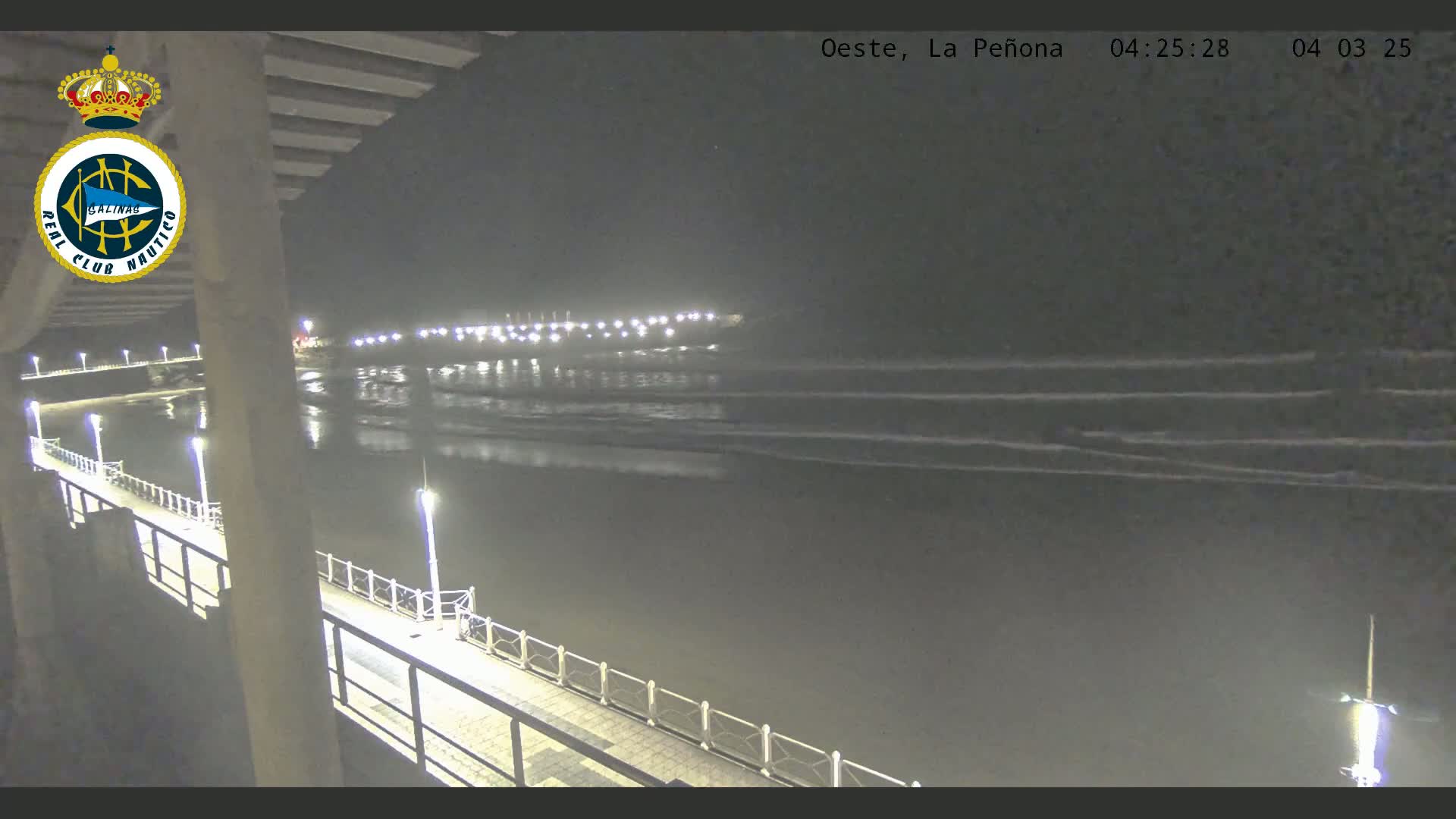 A nighttime view from a pier shows gently lapping waves on a dark ocean under a clear sky.